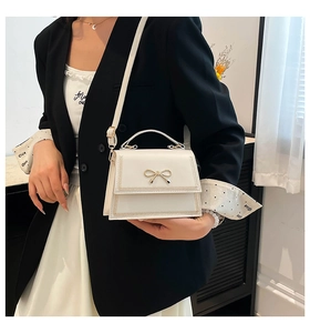 Primer plano de un elegante bolso bandolera blanco con lazo dorado y costuras finas.