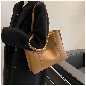 Brown leather tote bag styled with a black coat in a minimalist indoor studio setting