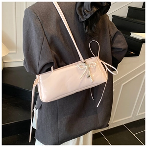 Detail of pink patent leather shoulder bag with pearl bow on a female model back