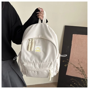Détail d'un sac à dos blanc en nylon avec écusson smiley jaune et tirette de zip tressée