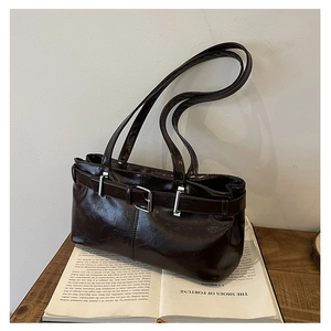Detail of vintage dark brown glossy leather underarm bag with silver buckle on a book