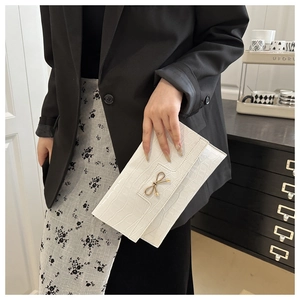 Close-up of white croc-embossed PU leather clutch with golden bow metal clasp detail