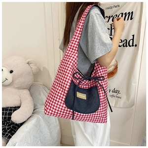 Detail of red checkered canvas tote bag with denim pocket and decorative bow on shoulder