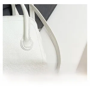 Gros plan du cuir grainé blanc perle avec coutures précises sur un petit sac carré