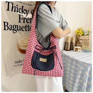 Detail of red checkered canvas tote bag with denim pocket and blue drawstring bow detail