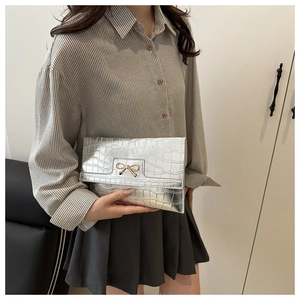 Detail of silver crocodile-embossed clutch bag featuring a golden bow-knot metal clasp