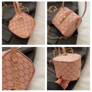 Detail view of pink mini cylinder bag with M-pattern leather texture and gold chain strap