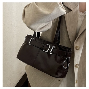 Detail of dark glossy leather shoulder bag with silver buckle and sleek texture on blazer