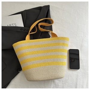 Detail of yellow and white striped straw tote bag with wide flat handles on textured fabric