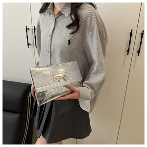 Detail of silver crocodile pattern PU leather clutch bag with golden bow metallic buckle