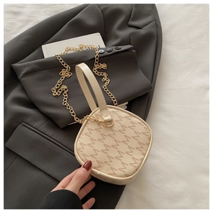 Detail of cream monogram crossbody bag with gold chain strap on grey blazer background