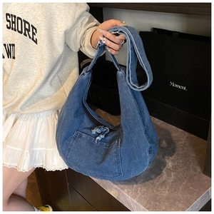 Detail of blue denim hobo bag with front patch pocket and wide strap held by model
