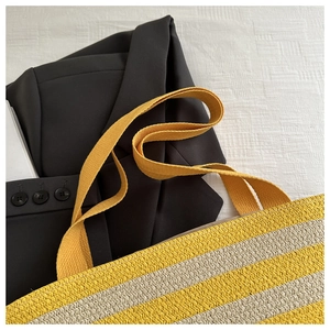 Detailed macro shot of yellow and beige striped woven straw tote bag with canvas handles