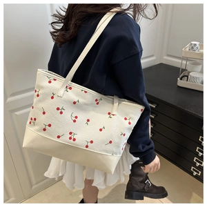 Detail view of beige corduroy tote bag featuring red cherry patterns and leather base