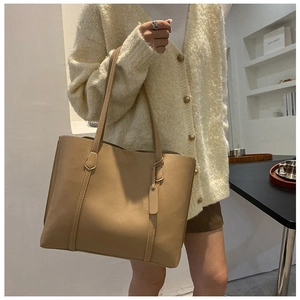 Close-up of khaki tote bag featuring slim shoulder straps and a matching luggage tag charm