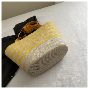 Detail of handwoven straw bucket bag with yellow stripes and broad fabric shoulder strap