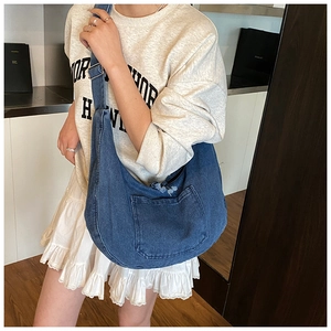 Detail of a navy denim crescent crossbody bag with utility pocket and adjustable strap