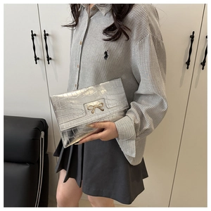 Detail of silver stone-textured PU clutch featuring a gold metallic bow buckle closure