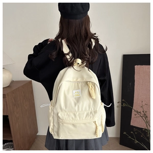 Detail of cream backpack showing smiling face patch and side drawstring adjustments