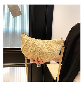 Detailed texture of beige woven crescent bag with golden bow ornament and slim strap