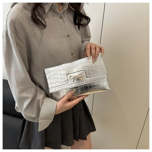 Detail of silver crocodile pattern clutch bag featuring a gold metal bow buckle