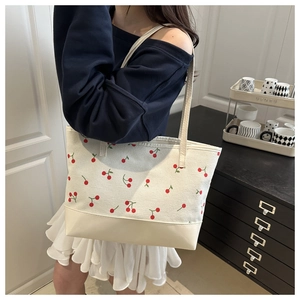 Détail du sac fourre-tout en toile à motifs de cerises rouges et fond en cuir beige