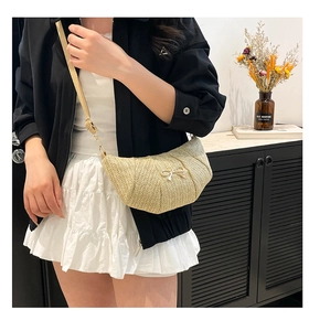 Detail of beige woven crescent bag with gold bow ornament worn as crossbody style