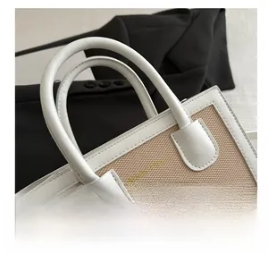 Detail of a color-block handbag showing white leather handles and beige woven texture