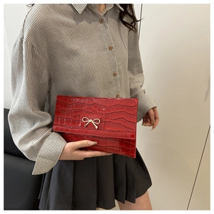 Close-up of red crocodile pattern clutch bag featuring a gold bow metallic detail