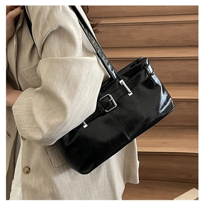 Detail of a black glossy leather shoulder bag with vintage buckle straps on a model