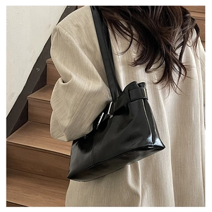 Detail of a glossy black underarm bag with silver buckle worn with a beige blazer