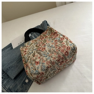 Close-up of floral knit tote bag with black handles next to an art book and denim jacket