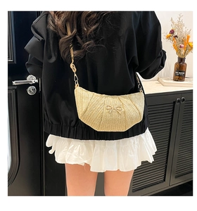 Close-up of beige woven crossbody bag with bow detail on female model in outfit