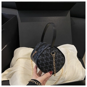 Detail of black cylindrical handbag with blue M print and golden chain strap in a box