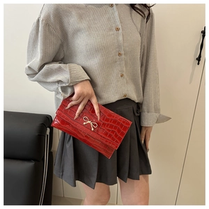 Detail of red crocodile textured clutch bag with a golden metal bow buckle decoration