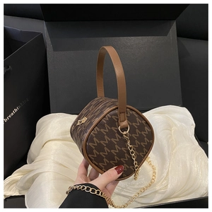 Macro view of brown leather bag featuring M pattern and gold chain strap detail