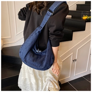 Detail of a large dark blue denim hobo bag with a decorative pocket and raw edges