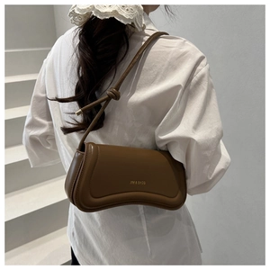 Detail view of a brown leather curved shoulder bag featuring a knotted strap and gold logo