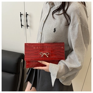 Detailed macro view of red crocodile-patterned PU clutch featuring a gold bow buckle