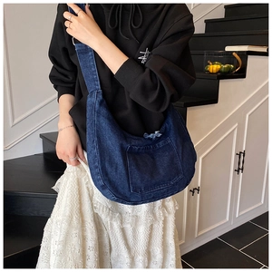 Close-up of a dark blue denim crossbody dumpling bag featuring a large front pocket