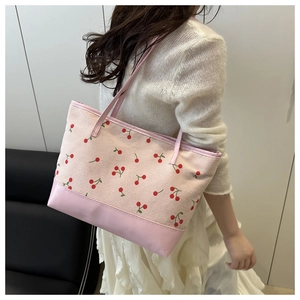 Pink corduroy tote bag with red cherry print and leather bottom shown on shoulder