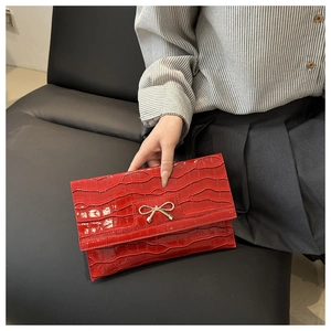Detail of red crocodile texture envelope bag with gold bow clasp held by a model