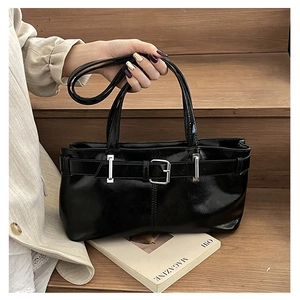 Detailed view of black patent leather shoulder bag with metal buckle on wooden stairs