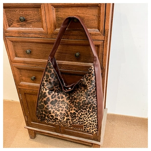 Détail d'un sac cabas imprimé léopard avec bandoulière en cuir marron sur commode bois
