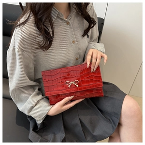 Detail of red crocodile pattern envelope clutch featuring a golden bow metal buckle