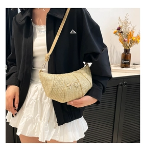 Detail of straw woven croissant bag with metal bow accent and slim strap on model