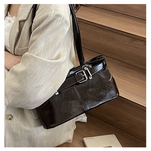 Detail of dark brown patent leather underarm bag with decorative metal buckle and strap