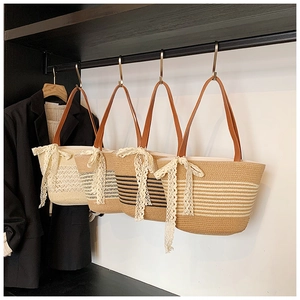 Detail view of woven straw shoulder bags with leather straps and delicate lace bows