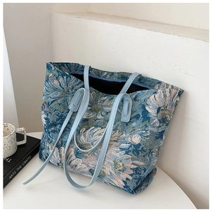 Artistic oil painting style floral tote bag with blue leather straps on a white desk