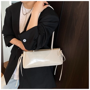 Detail of cream glossy shoulder bag with bow accents on model in dark blazer